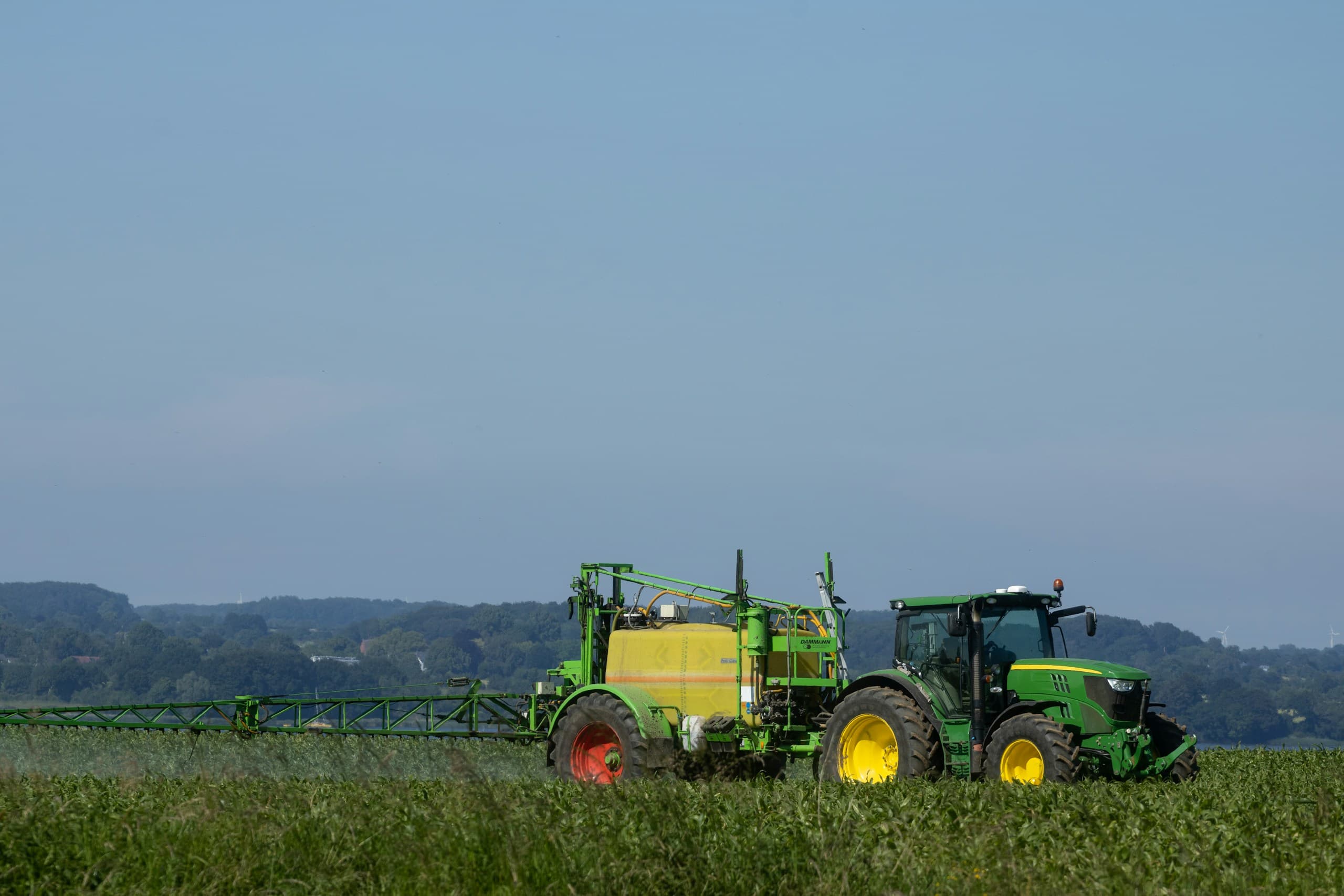 Traktor mit Anhängespritze auf einem Feld vor bewaldeten Hügeln